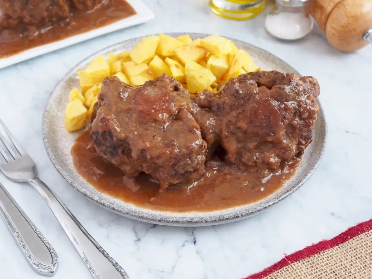 Dos trozos de rabo de toro guisado en salsa, acompañados de patatas fritas. Un plato tradicional listo para disfrutar.