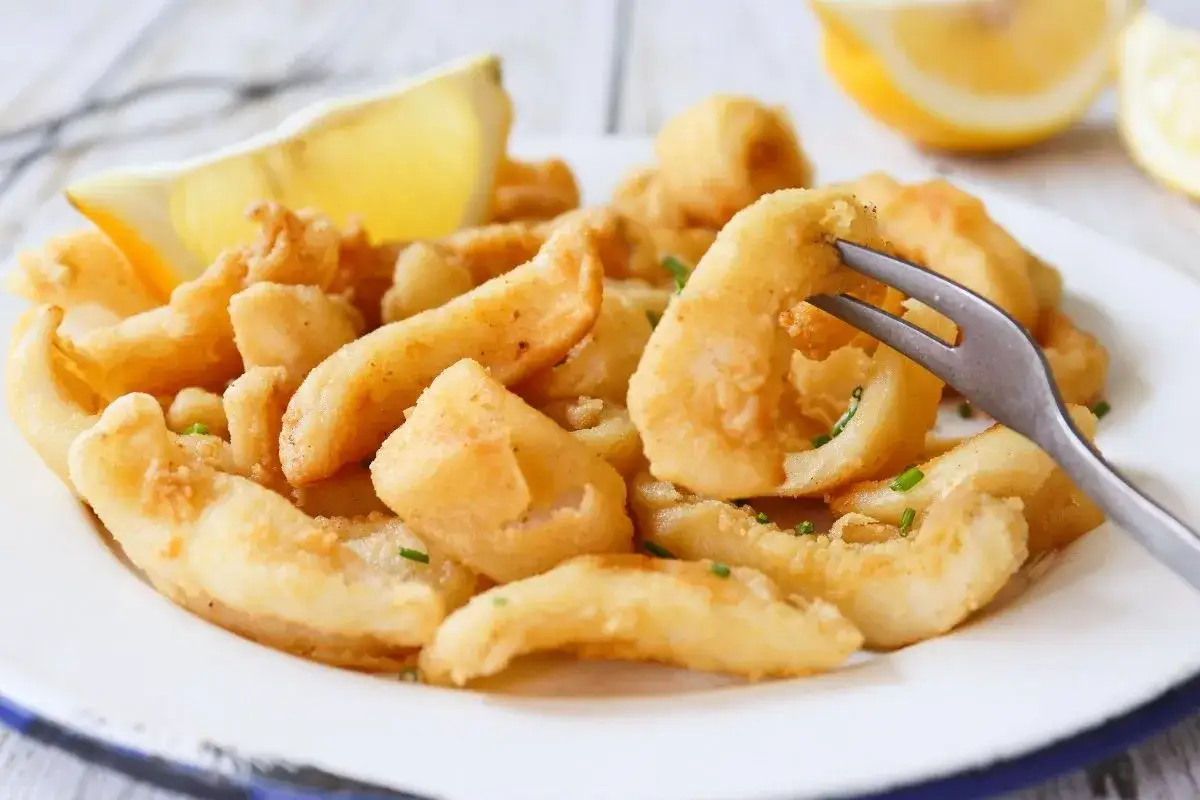 Un plato de chocos fritos crujientes, adornado con gajos de limón y perejil picado. Un tenedor se alza listo para probar esta delicia.