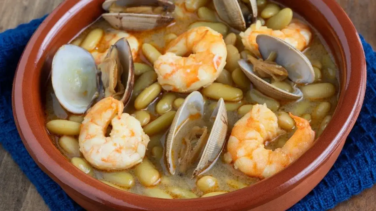 Plato de fabes con almejas y gambas, servido en cazuela de barro.