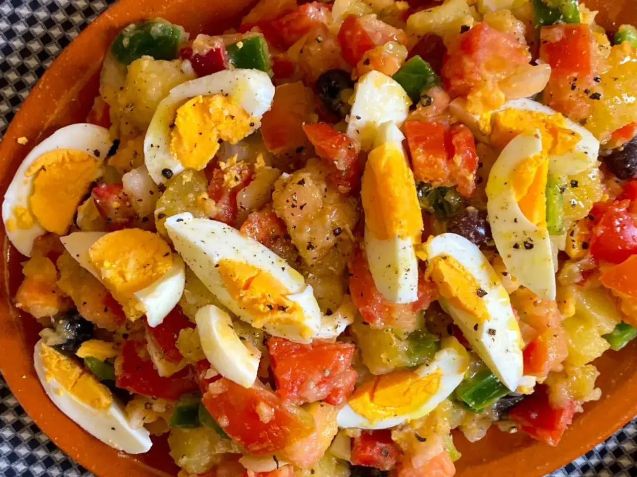 Deliciosa amanida de patata con trozos de huevo duro, tomate, pimiento verde y aceitunas negras.