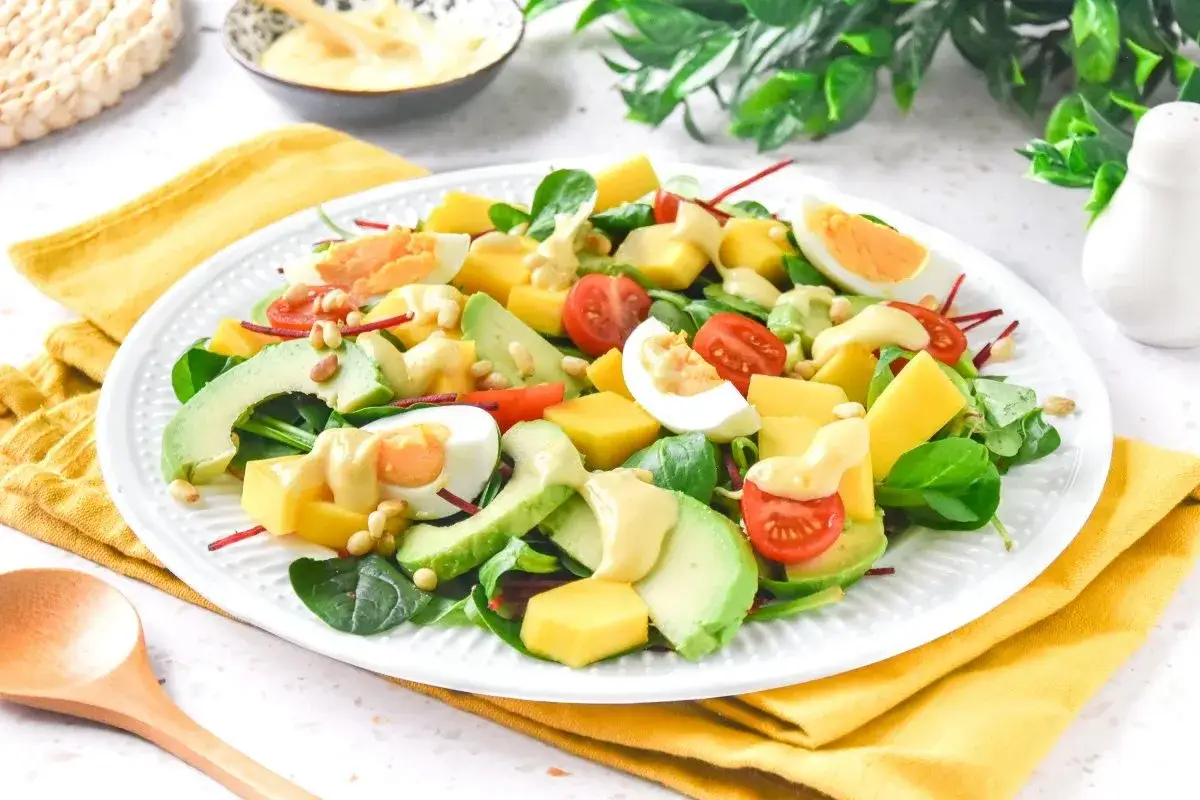 Ensalada de mango con aguacate, huevo duro, tomates cherry y pi&ntilde;ones, aderezada con una cremosa salsa.