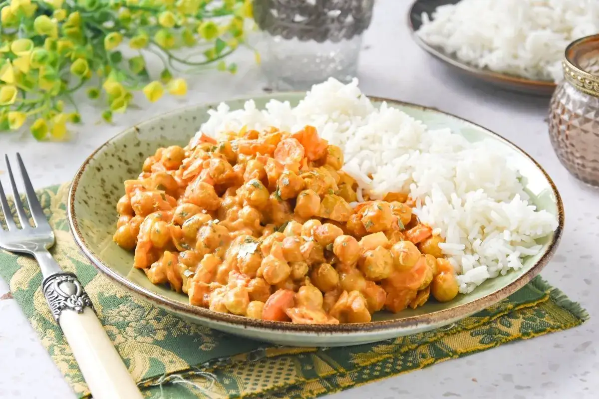 Un plato de garbanzos con arroz, cubierto con una cremosa salsa naranja y decorado con perejil picado.