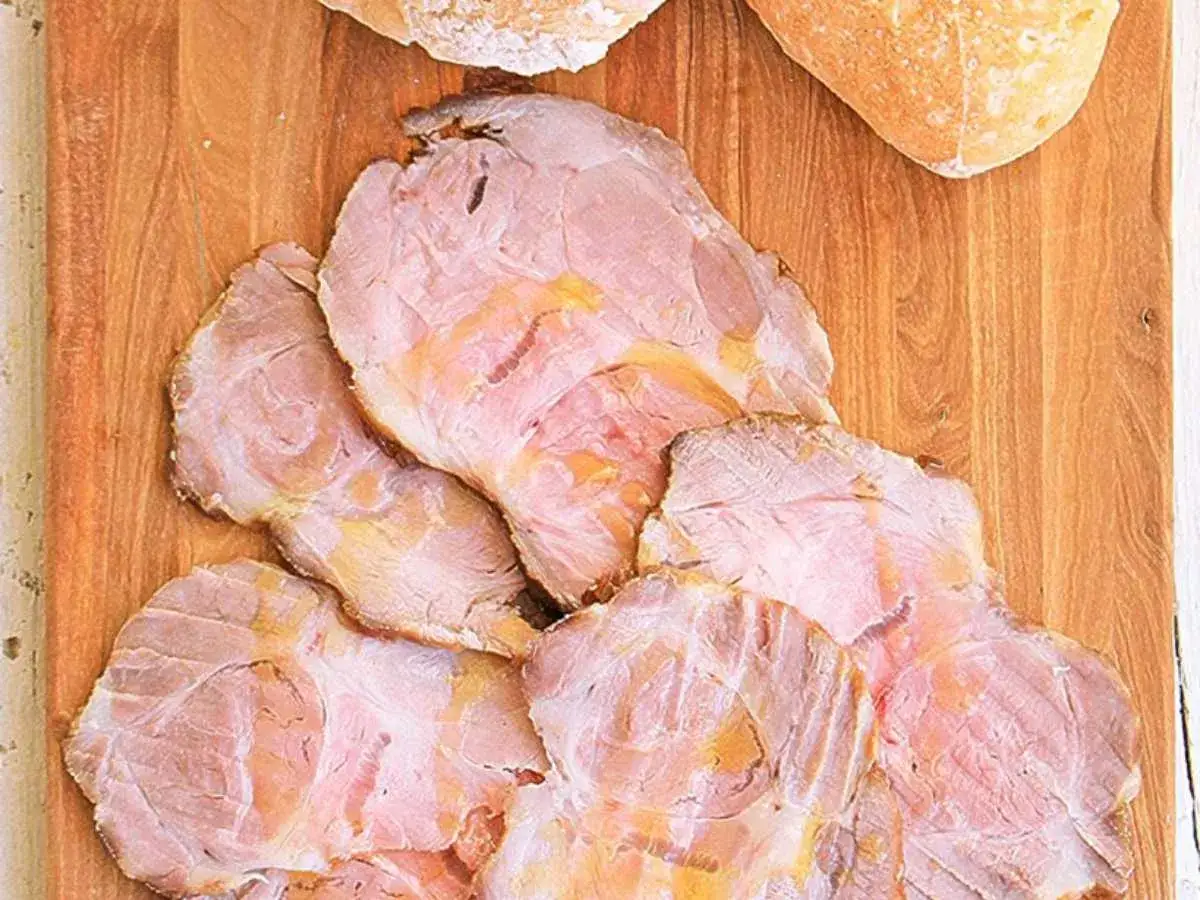 Lonchas de jugosa carne mechada, tierna y rosada, dispuestas sobre una tabla de madera junto a pan rústico.