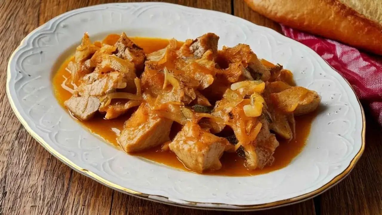 Sabroso at&uacute;n encebollado en una salsa dorada, servido en un plato blanco con borde dorado.