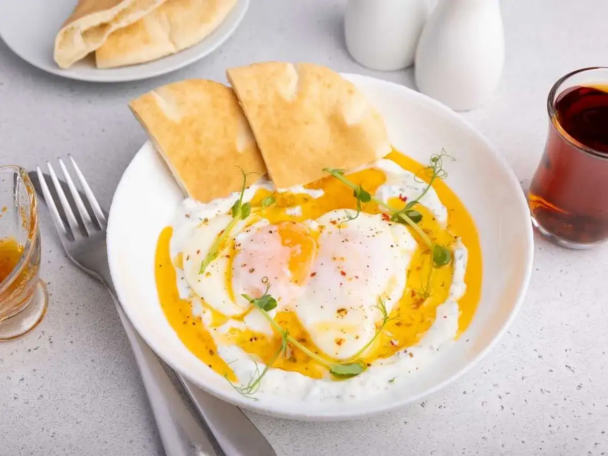 Deliciosos huevos turcos con yogur cremoso, pan de pita y un toque de hierbas frescas.