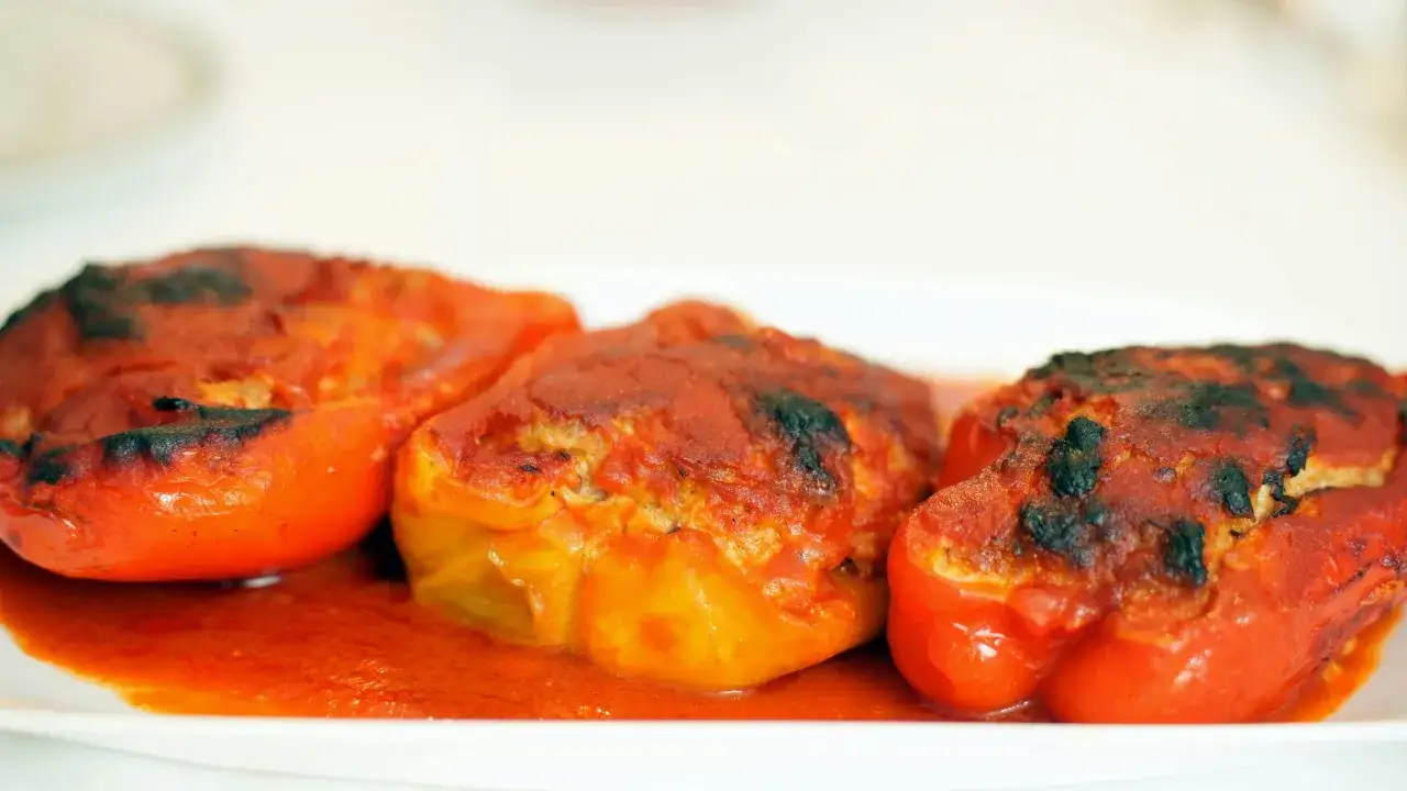 Tres pimientos rellenos, cubiertos de salsa de tomate y horneados hasta dorar, reposan en un plato blanco.