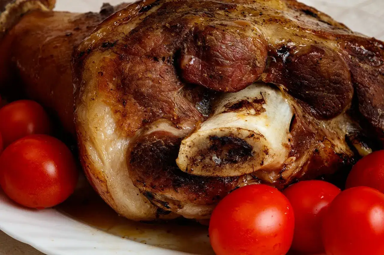 Codillo de cerdo asado, jugoso y dorado, acompa&ntilde;ado de tomates rojos frescos.