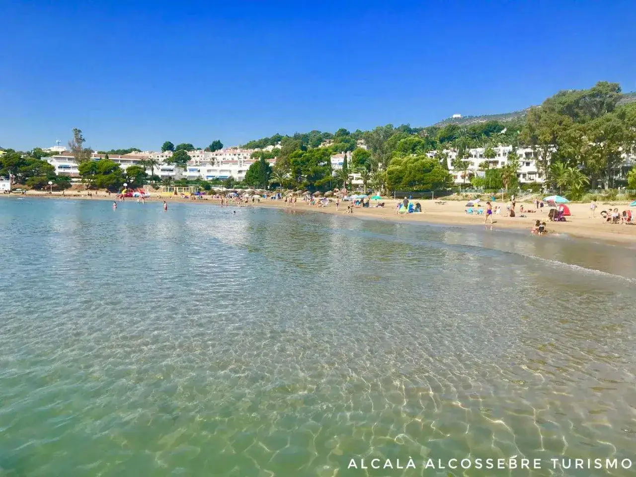 Aguas cristalinas en la cala blanca, con gente disfrutando del sol y el mar en una playa mediterránea.