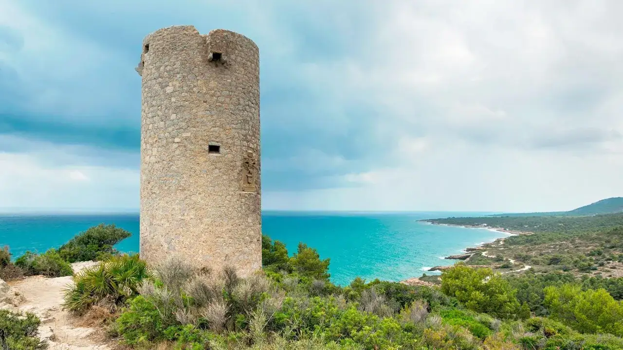 Torre defensiva en la playa del Russo, Peñíscola, con el mar turquesa y vegetación mediterránea.