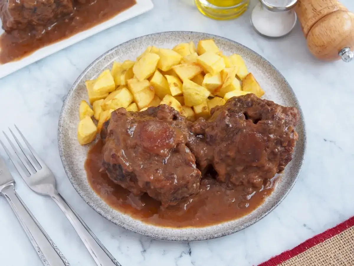 Dos trozos de rabo de ternera en salsa, acompa&ntilde;ados de patatas fritas crujientes. Un plato tradicional listo para disfrutar.
