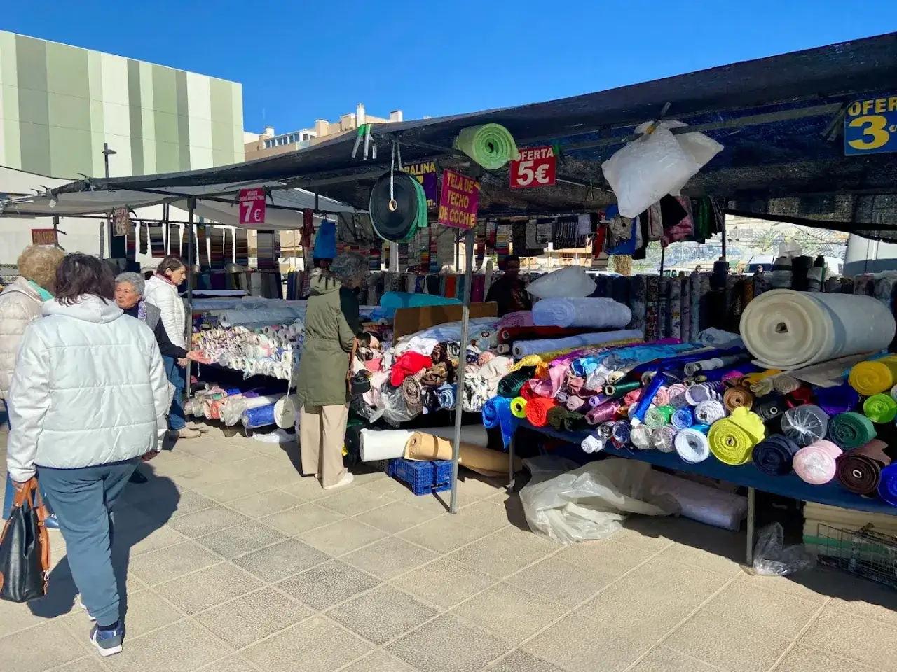 Gente comprando telas de colores en el mercadillo semanal Benicarl&oacute;. Rollos de tela para costura y tapicer&iacute;a.