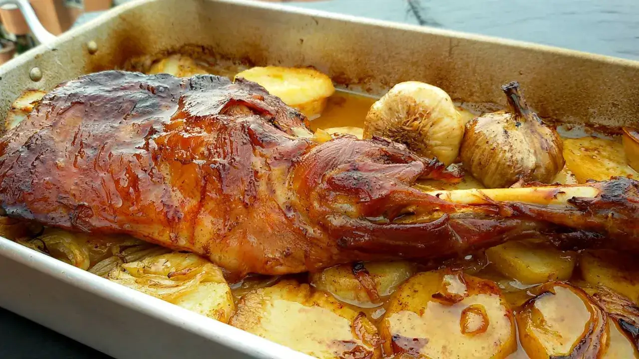 Paletilla de cordero al horno, dorada y jugosa, acompa&ntilde;ada de patatas y ajos asados en su jugo.