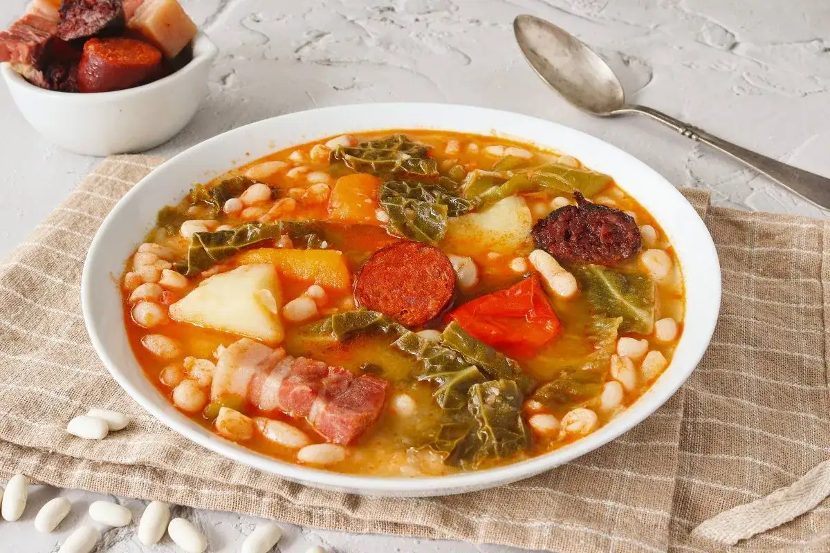 Un reconfortante cocido monta&ntilde;&eacute;s, con garbanzos, chorizo, morcilla, tocino y verduras, servido en un plato blanco.