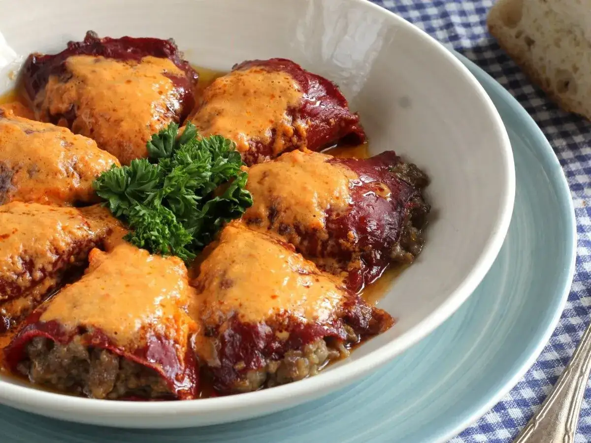 Pimientos rellenos de carne de la abuela, cubiertos con una cremosa salsa y decorados con perejil. Un plato casero que evoca recuerdos.