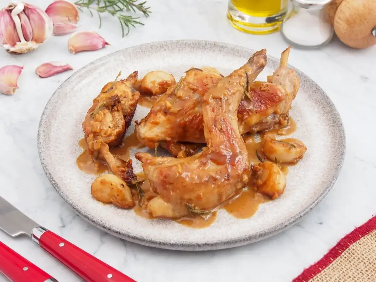 Delicioso conejo al ajillo servido en un plato, con trozos de ajo dorado y romero.