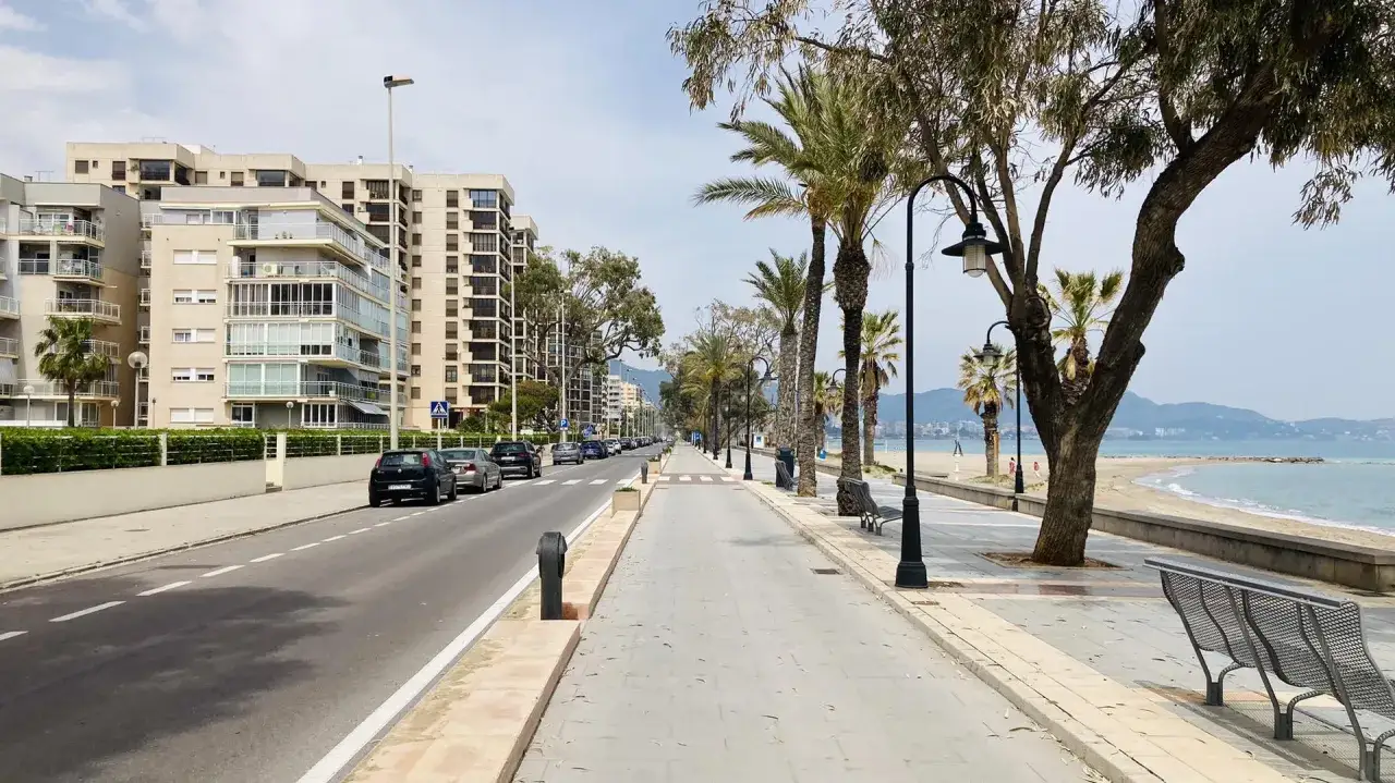 Un día tranquilo en el paseo marítimo de Benicàssim, con edificios modernos a un lado y la playa y el mar al otro.