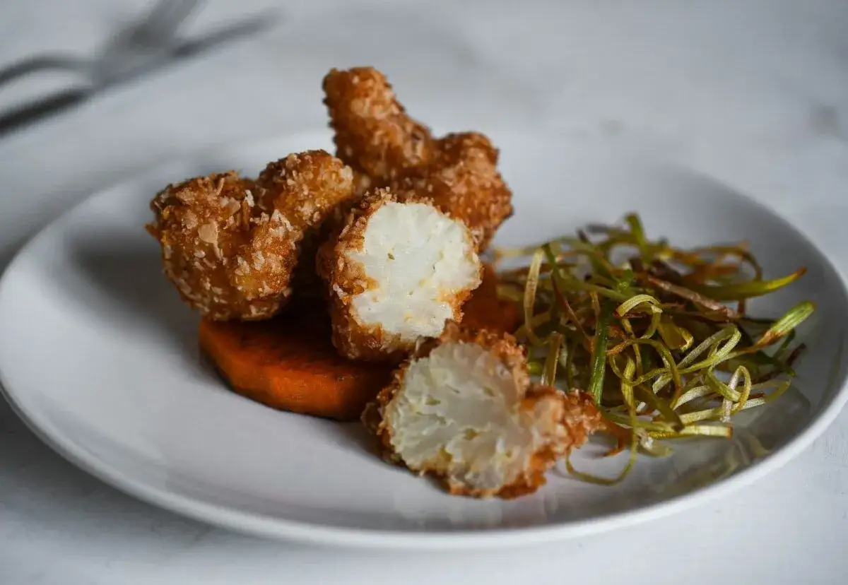 Crujiente coliflor rebozada, servida sobre pur&eacute; de calabaza y acompa&ntilde;ada de puerros fritos.