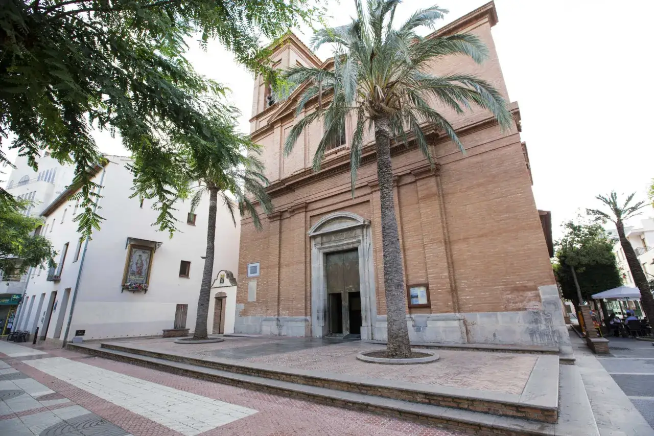 Iglesia en el casco antiguo Benic&agrave;ssim pueblo, con palmeras y una calle peatonal.