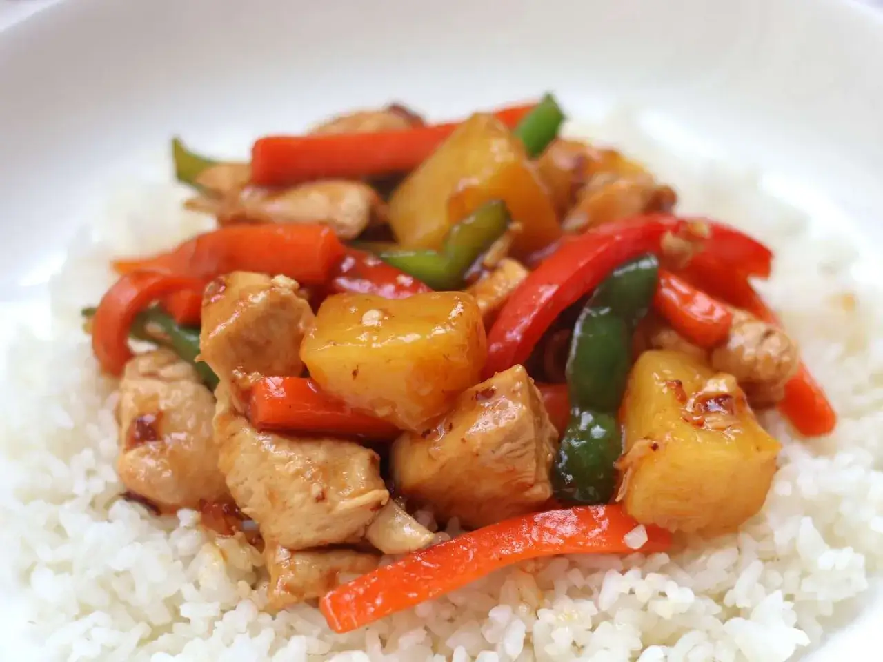 Sabroso pollo agridulce con trozos de pi&ntilde;a, pimientos rojos y verdes sobre una cama de arroz blanco.