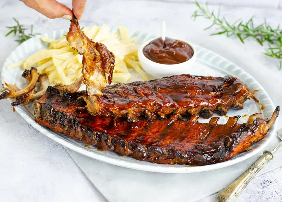 Costillas a la barbacoa jugosas y glaseadas, servidas con patatas fritas y salsa.