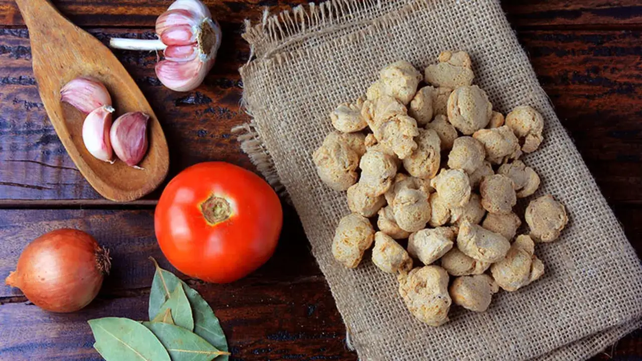 Un mont&iacute;culo de soja texturizada sobre arpillera, junto a un tomate, cebolla, ajos y hojas de laurel. Ingredientes para una deliciosa comida.