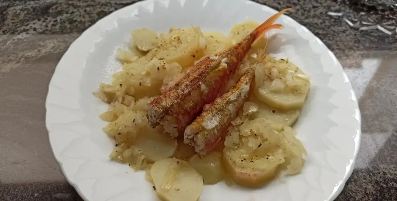 Dos salmonetes al horno, dorados y jugosos, reposan sobre una cama de patatas y cebolla tierna.