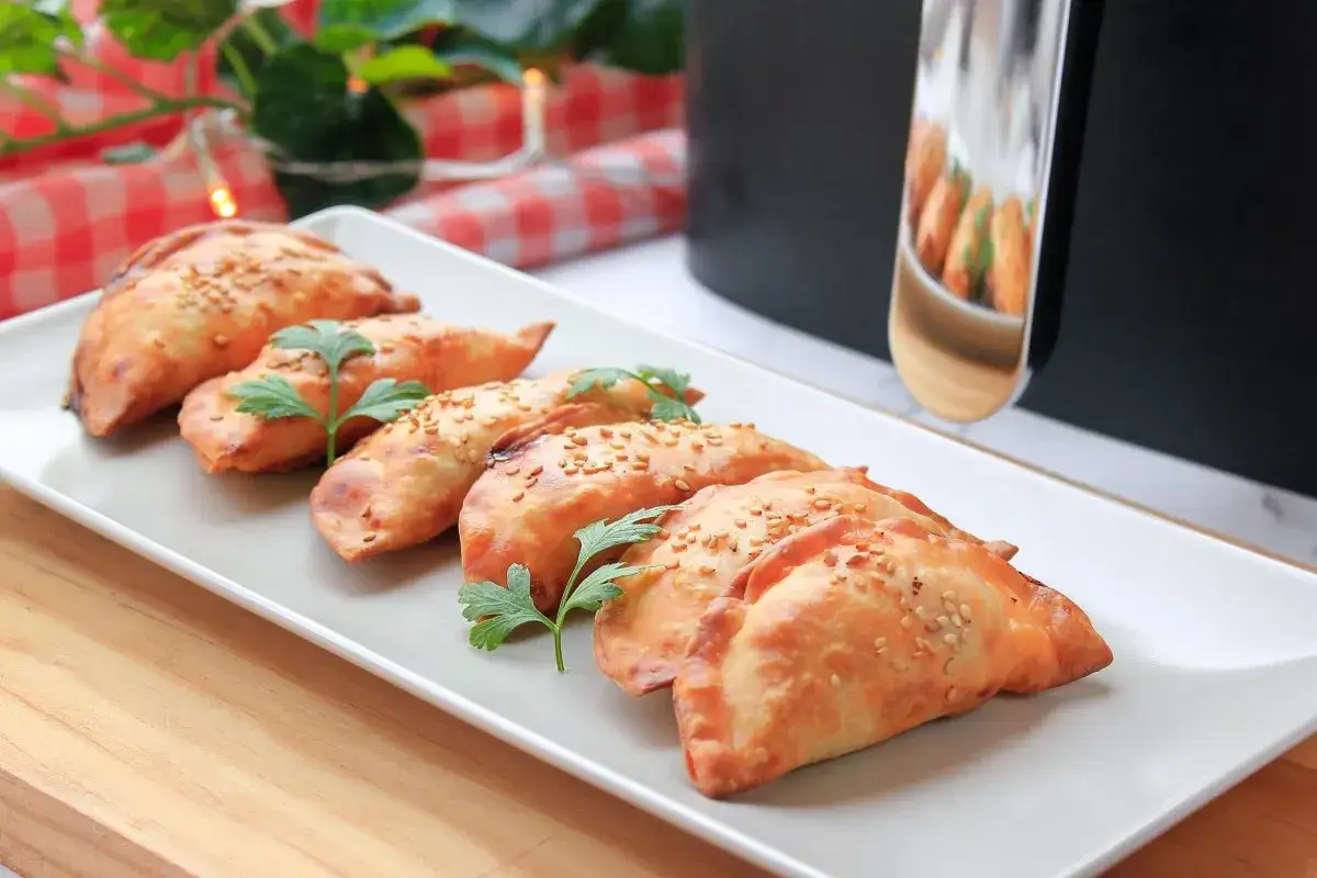 Deliciosas empanadillas en freidora de aire, doradas y crujientes, espolvoreadas con semillas de s&eacute;samo y perejil fresco.
