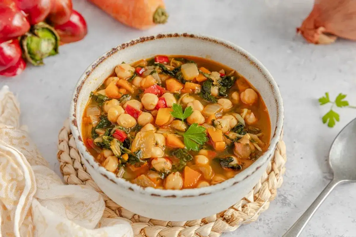 Un taz&oacute;n humeante de garbanzos con verduras, lleno de zanahoria, espinaca y pimiento rojo. Un plato reconfortante y saludable.