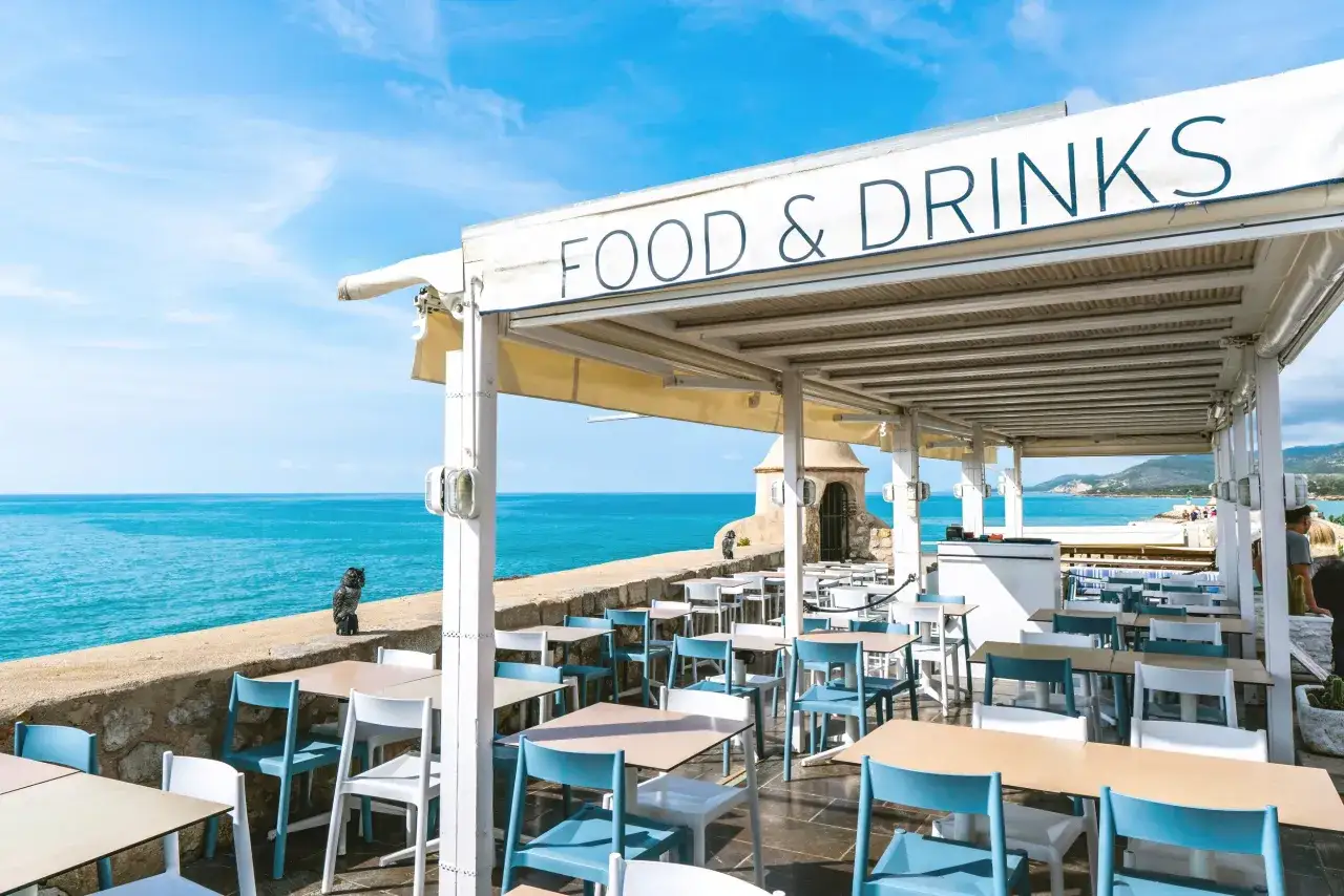 Terraza de restaurante con vistas al mar. Mesas y sillas azules y blancas listas para recibirte. &iexcl;El lugar perfecto donde comer en Pe&ntilde;&iacute;scola!