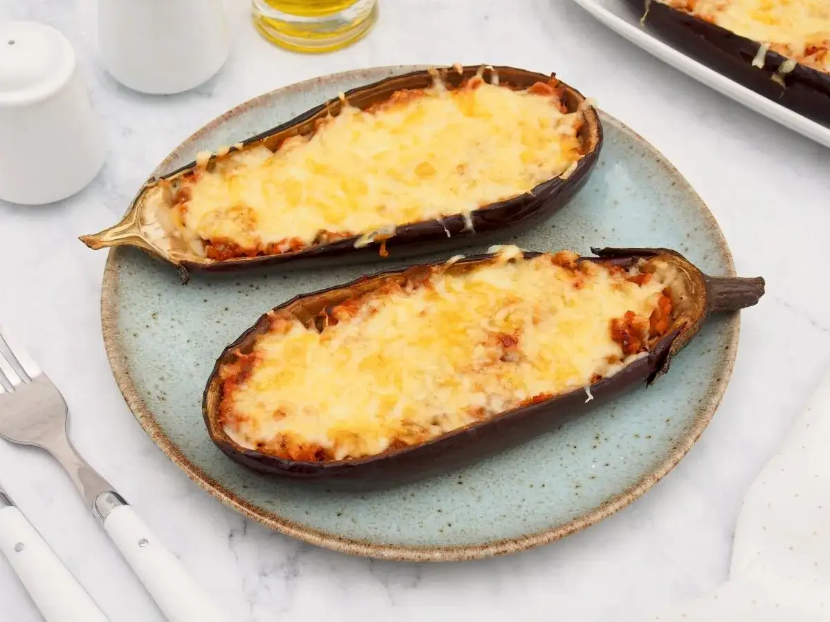 Dos mitades de berenjenas rellenas de at&uacute;n y gratinadas con queso, servidas en un plato azul.