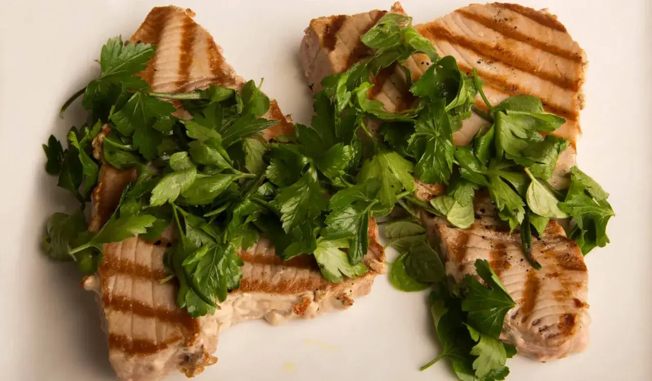 Dos filetes de at&uacute;n a la plancha, con marcas de parrilla y cubiertos con perejil fresco.