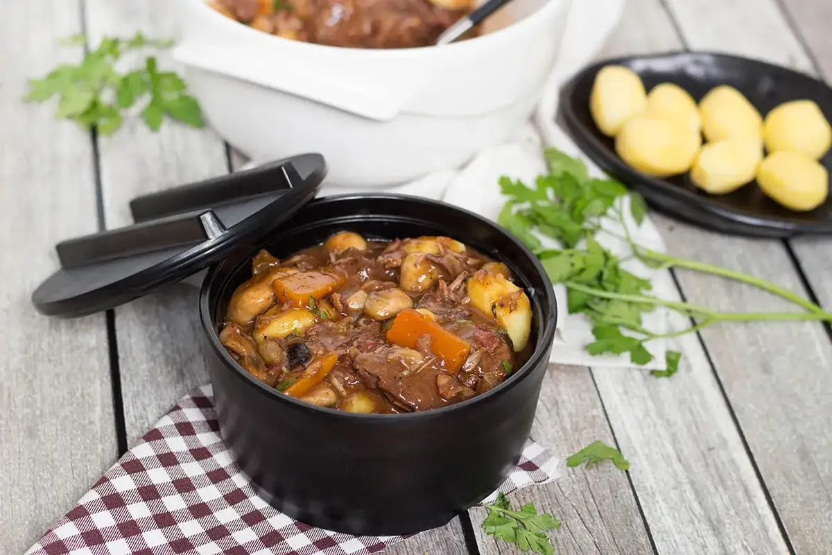 Un delicioso boeuf bourguignon humea en una olla negra, acompa&ntilde;ado de patatas cocidas y perejil fresco.