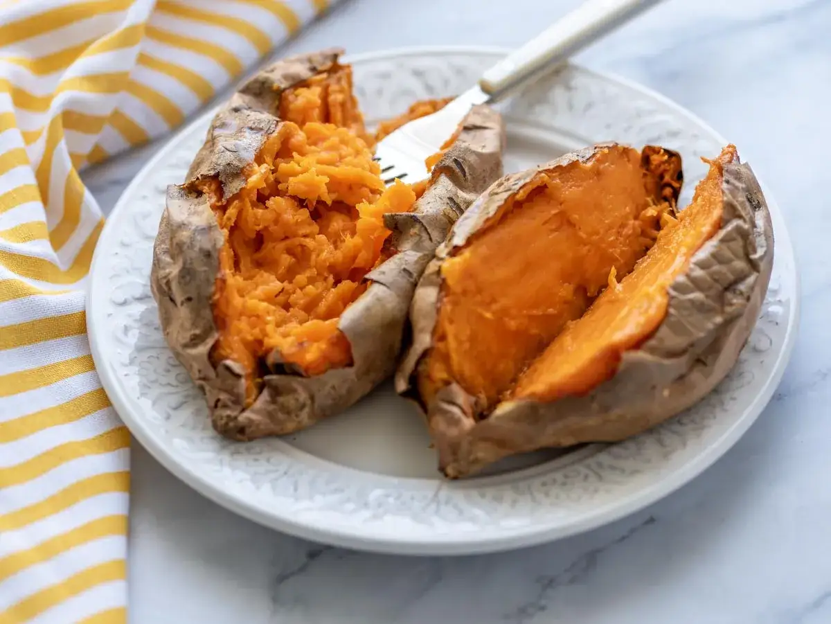 Boniato tierno y esponjoso hecho en air fryer, servido en plato blanco con un tenedor.
