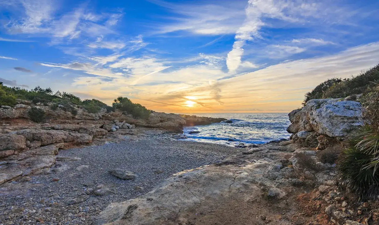 Atardecer en una cala rocosa de Alcossebre. El sol se pone sobre el mar Mediterr&aacute;neo, pintando el cielo de tonos naranjas y azules. Un lugar perfecto que ver en Alcossebre.
