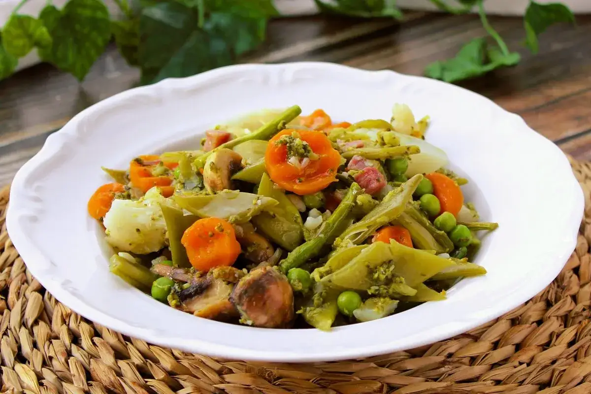 Un plato de menestra de verduras con zanahoria, jud&iacute;as verdes, guisantes, champi&ntilde;ones y patatas, todo aderezado con una salsa verde.