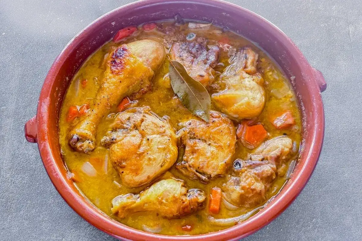 Un delicioso pollo guisado en cazuela de barro, con trozos dorados de pollo, zanahorias y una hoja de laurel.