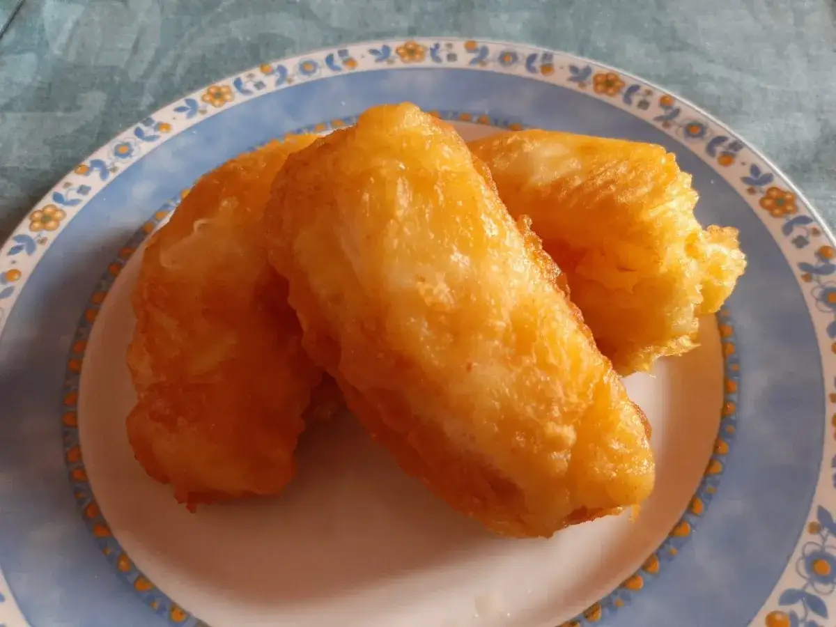 Tres trozos de bacalao rebozado, dorados y crujientes, servidos en un plato con borde azul y decorado con flores.
