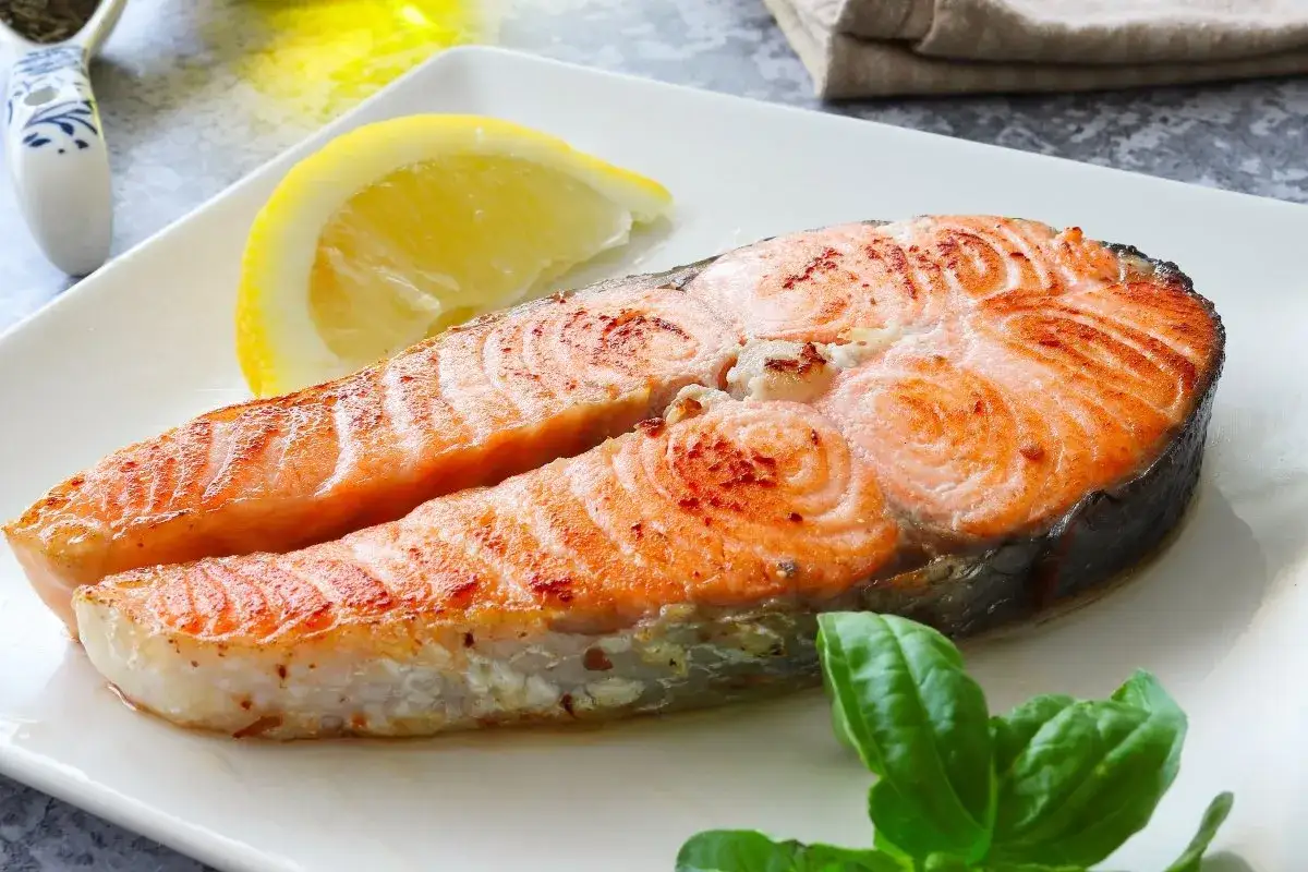 Un jugoso salm&oacute;n a la plancha, dorado y tierno, servido con una rodaja de lim&oacute;n y hojas verdes.