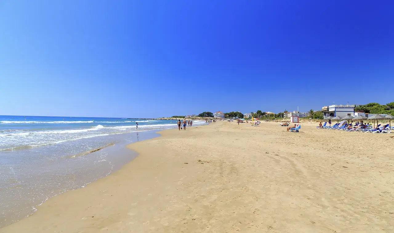 Playa de Alcossebre con gente paseando y tumbonas bajo sombrillas. Un d&iacute;a perfecto para saber qu&eacute; hacer en Alcossebre.