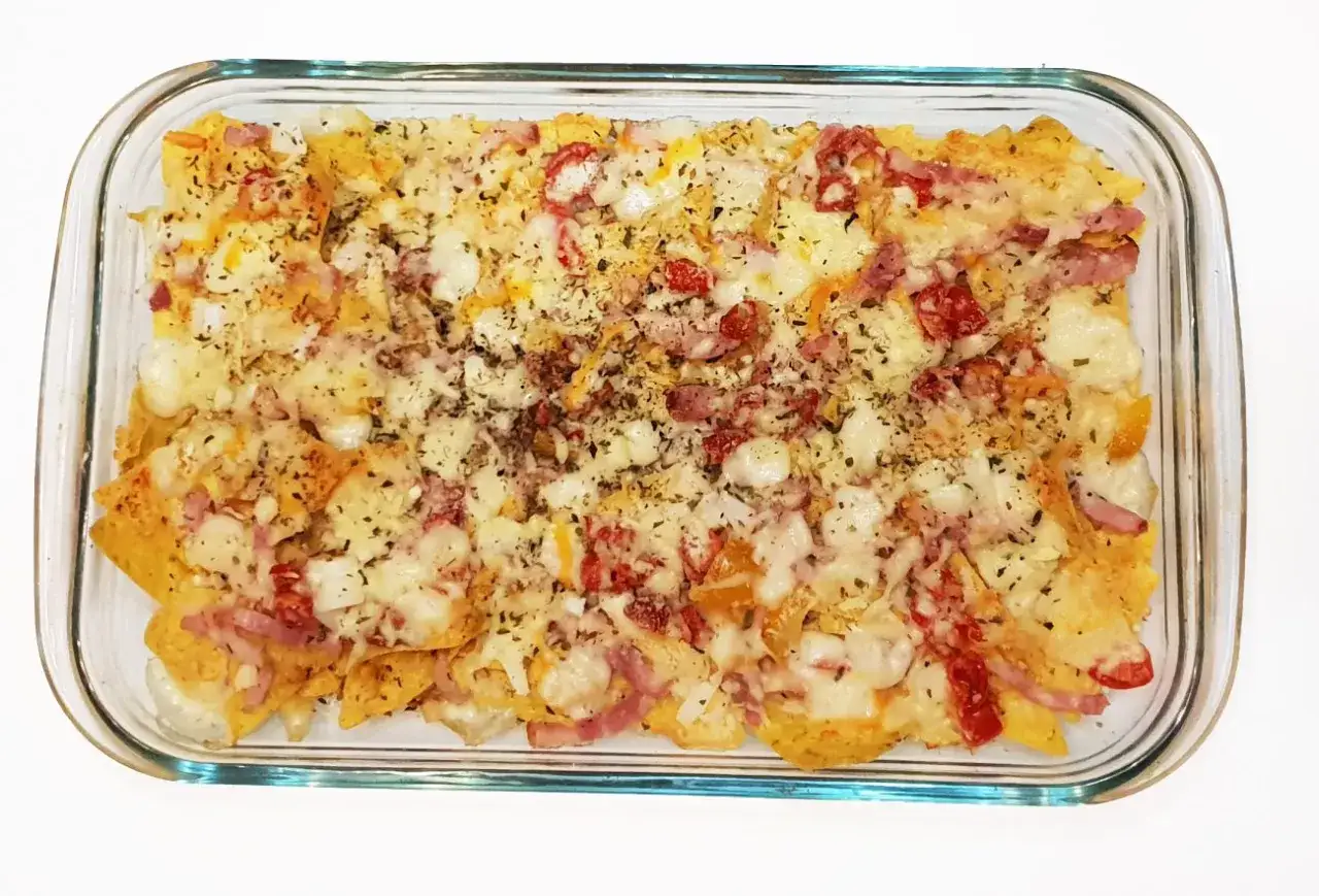Nachos con queso fundido, trocitos de jam&oacute;n y tomate, espolvoreados con hierbas. &iexcl;Un antojo irresistible!