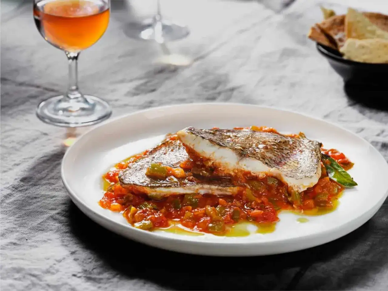Deliciosa urta a la rote&ntilde;a servida en plato blanco, con un vaso de vino y pan tostado al fondo.