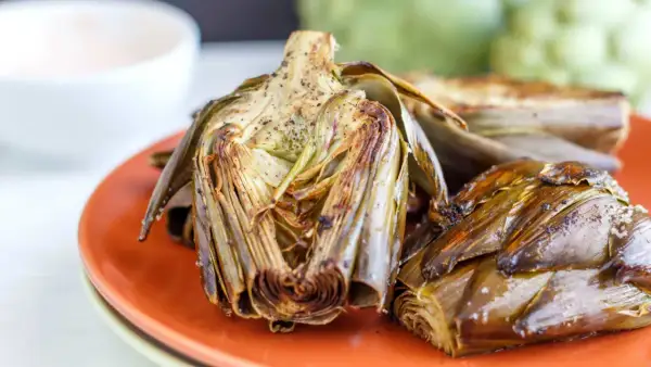 Deliciosas alcachofas al horno, doradas y tiernas, servidas en un plato naranja. Perfectas para disfrutar de su sabor.