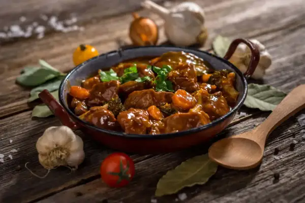 Un delicioso ragout de ternera, con trozos de zanahoria y brócoli, servido en una sartén rústica. Acompañado de ajo, tomate y laurel.