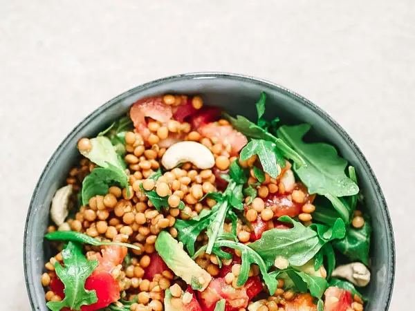 Deliciosa ensalada de lentejas con aguacate, tomate y rúcula, coronada con anacardos. Un plato fresco y nutritivo.