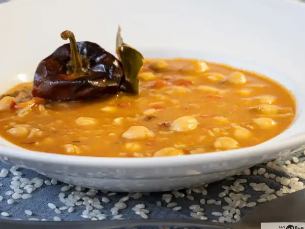 Un plato humeante de garbanzos con arroz, decorado con un pimiento seco y una hoja de laurel.