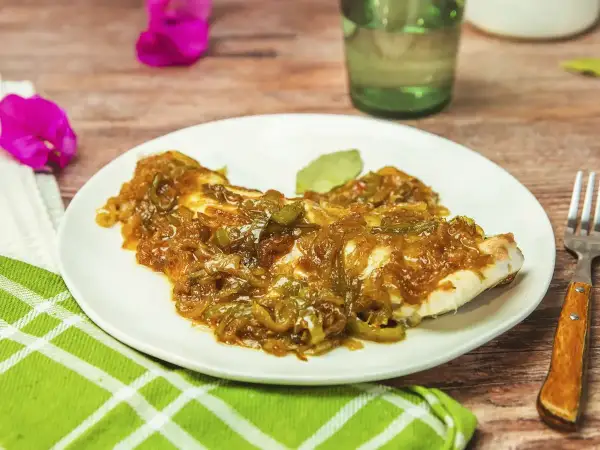 Un plato de urta a la roteña, con su jugoso pescado cubierto de cebolla y pimientos caramelizados, listo para disfrutar.
