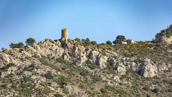 Torreón solitario en la cima rocosa del Desierto de las Palmas, vigilando un paisaje árido y escarpado bajo un cielo azul.