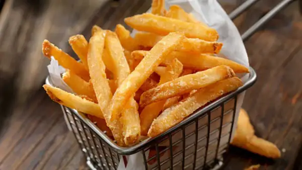 Cesta metálica llena de crujientes patatas fritas al horno, servidas sobre papel blanco.