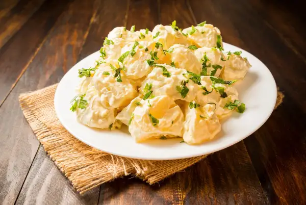 Patatas alioli cremosas y deliciosas, cubiertas con perejil fresco, servidas en un plato blanco sobre una mesa de madera rústica.
