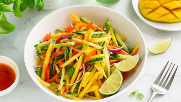Ensalada de mango vibrante con pepino, zanahoria, cebolla morada y pimientos, aderezada con lima.